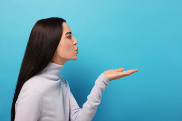 Beautiful young woman blowing kiss on light blue background. Space for text