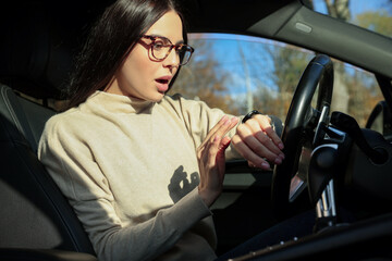 Fototapeta na wymiar Emotional woman checking time on watch in car. Being late concept
