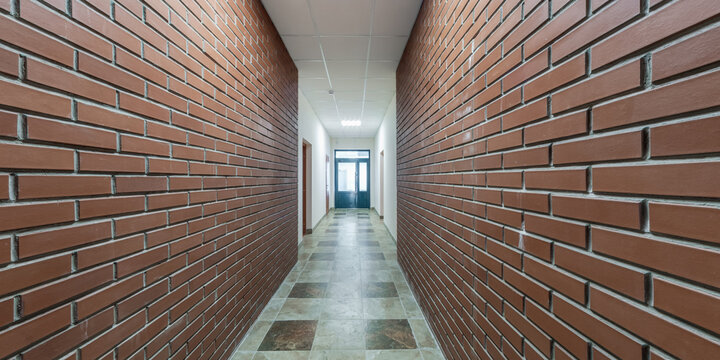 panorama in empty long corridor with red brick walls and doors in interior of modern office