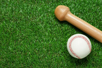 Wooden baseball bat and ball on green grass, flat lay. Space for text