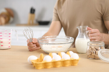 Man with whisk and different ingredients at table in kitchen, closeup. Online cooking course