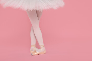 Young ballerina in pointe shoes practicing dance moves on pink background, closeup. Space for text