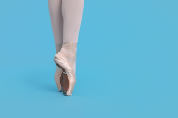 Young ballerina in pointe shoes practicing dance moves on light blue background, closeup. Space for text