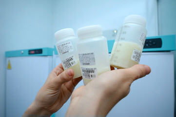 Lab assistant hand holding breast milk storage containers with human milk, freezers on a...