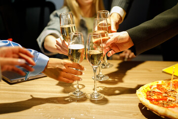 Successful business people are clinking glasses of champagne and smiling while celebrating in office