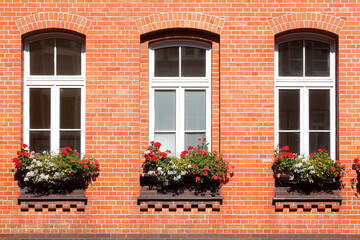 Fototapeta na wymiar Fenster mit Blumenkästen an einer rötlichen Hausmauer aus Backstein, Wunstorf, Niedersachsen, Deutschland