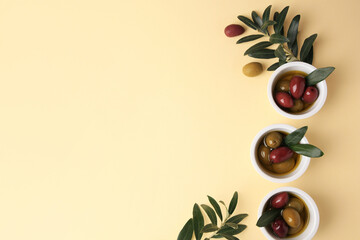 Bowls with different ripe olives and leaves on beige background, flat lay. Space for text