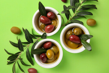 Bowls with different ripe olives and leaves on light green background, flat lay