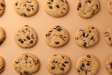 Many delicious chocolate chip cookies on beige background, flat lay