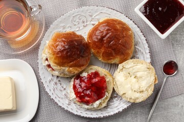 Freshly baked soda water scones with cranberry jam, butter and cup of tea on light grey table, flat lay