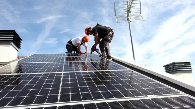 A team of Hispanic technicians install solar panels on the roof of a house. Cross section view of builder in helmet installing renewable energy solar panel system concept