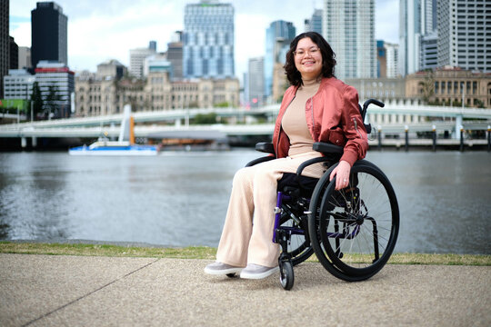 Smiling woman in wheelchair in front of river with city in background