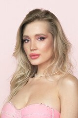 Fototapeta premium A beautiful attractive woman with blonde hair in a stunning pink dress on a pink background. Fashion, beauty.