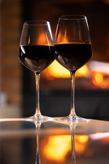 deux verres de vin rouge posés sur une table avec en arrière plan un feu de cheminée. Reflet des verres sur la table. Concept de la convivialité à l'heure de l'apéritif