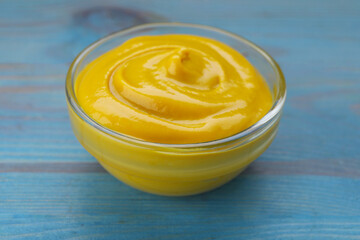 Sauce bowl with delicious mustard on light blue wooden table, closeup