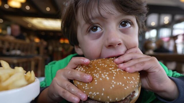 Happy kid eating hamburger. Child takes a bite of burger food meal