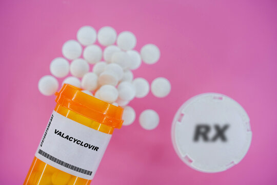 Valacyclovir Rx medicine pills in plactic vial with tablets. Pills spilling   from yellow container on pink background.