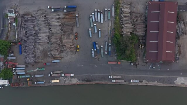 Timber waiting to be exported at port area along the Saigon river in Ho Chi Minh City, Vietnam. Traffic and buildings can be seen along the road. Top down aerial view from river to rooftops.