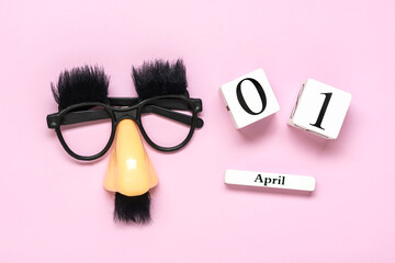 funny face - fake eyeglasses, nose and mustache, calendar with date 01 April on pink background Happy fools day concept 1st April party Holiday greetind card - 581784281