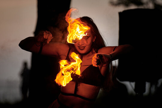 Girl fire dancing performance at outdoor art festival, smooth movements of female fire show artist with torch. Woman dancing with fire flame art performance, twilight forest background