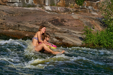 Cute mother bathes with a child in a turbulent stream of a mountain river