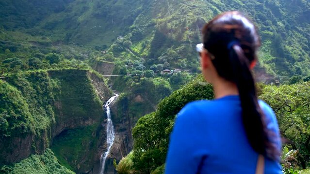 Woman from behind in blue sweater looking at Devil's Caudron waterfall. Ecuador. Static view