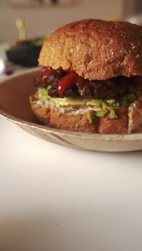 Hamburger brown bun sandwich with avocado, ketchup and red onion, vertical 4k shot