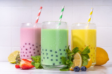 Set of three colorful summer bubble tea, bright creamy pearl tea or latte tapioca drinks, pink berry, yellow citrus, green mint, with tapioca balls and crushed ice, on white background