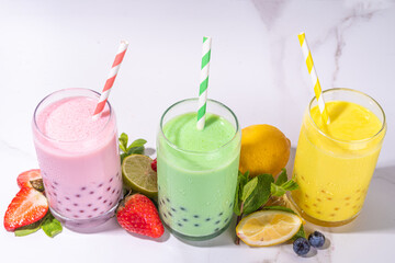 Set of three colorful summer bubble tea, bright creamy pearl tea or latte tapioca drinks, pink berry, yellow citrus, green mint, with tapioca balls and crushed ice, on white background