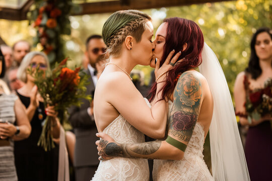 Two lesbian women in wedding dresses kissing at their wedding. Generative ai