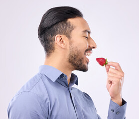 Healthy, diet and a man eating a strawberry in studio on a gray background for natural nutrition....
