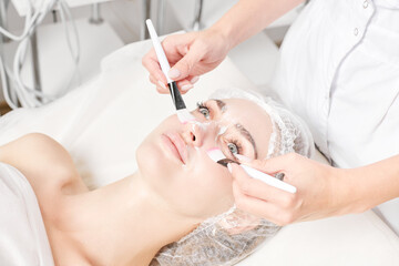 Beautician rubbing cream with brushes into female face skin for rejuvenation, moisturizing skincare...