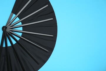 Stylish black hand fan on light blue background, top view. Space for text
