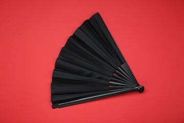 Stylish black hand fan on red background, top view