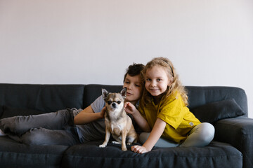 2 children sitting on the couch petting a small chihuahua dog, portrait, close up, lifestyle