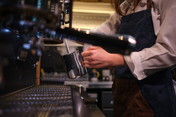Close up of a barista preparing milk for coffee on a espresso machine in coffee shop.