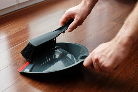 close-up of a man cleaning crumbs from the floor with a brush - Powered by Adobe