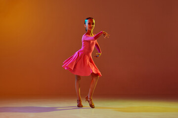 Studio shot of little girl, 11 years old kid in festive stage dress dancing ballroom dance over...