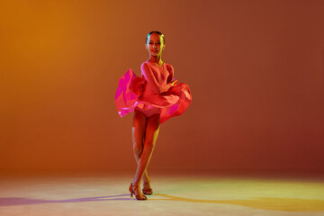 Studio shot of little girl, 11 years old kid in festive stage dress dancing ballroom dance over...