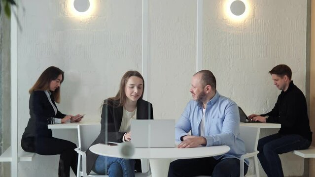 Business professionals, including freelancers and entrepreneurs, are working together in a room. Man and woman sitting together, collaborating on project using laptop, two other individuals entering.