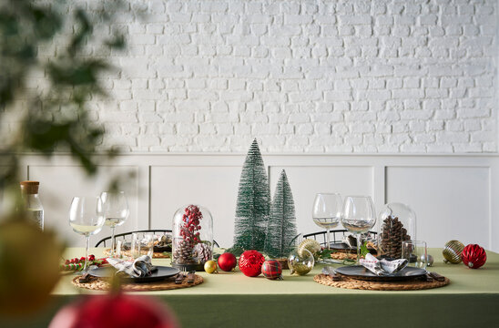 Christmas and new year dinner table serving, green tablecloth, accessory, tree, interior, white brick wall.