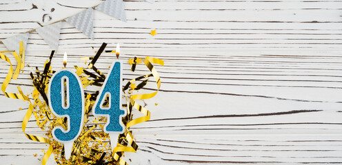 Number 94 blue celebration candle on white wooden background. Happy birthday for ninety-four years...