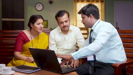 handheld shot of Banker showing insurance policy related details from laptop to couple at home - concept of financial advisor,