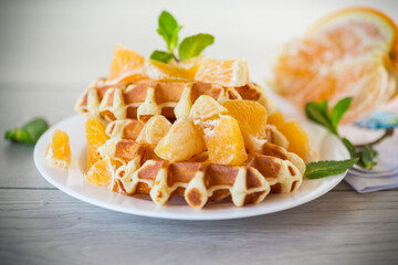 Cooked sweet Belgian waffles with oranges on the table.