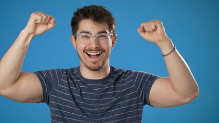 Shocked amazed say wow doing winner gesture put hands up young man 20s posing isolated on blue background studio. People lifestyle concept.