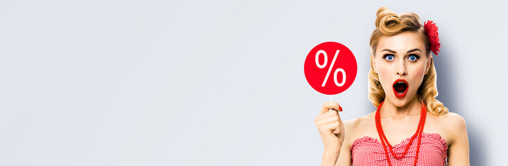 Face portrait of excited shocked woman with open mouth, hold red signboard with % sign. Blond pin up retro style girl. Isolated grey gray background. Sale ad concept. Wide image.