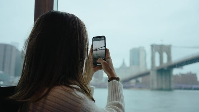 Girl taking a photo of the Brooklyn bridge from water taxi in New York
