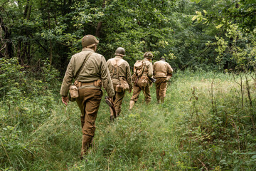 Historical reeneactors dressed As  american  Infantry Soldier during  World War II  patrol the forest. View from the back. Porąbka, Poland