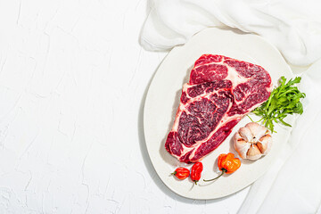 Raw Ribeye steak with spices and herbs. Dry aged meat, traditional food, hard light, dark shadow