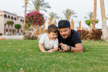 Portrait of cheerful young father lying on grass at park with her little baby son